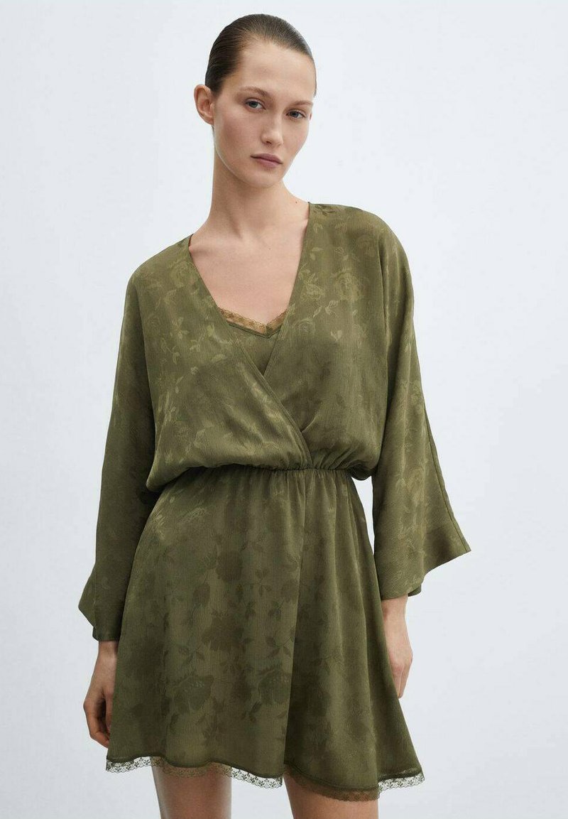 Robe vert olive au design croisé, avec des manches longues, une texture florale et un ourlet en dentelle. Superposée sur un débardeur avec des accents en dentelle.