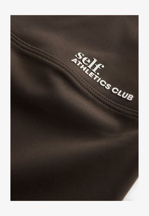 Schwarzer Sportstoff mit glatter Textur, versehen mit weißem Text: „self ATHLETICS CLUB“ an der Seitennaht und dezenten Stickdetails.