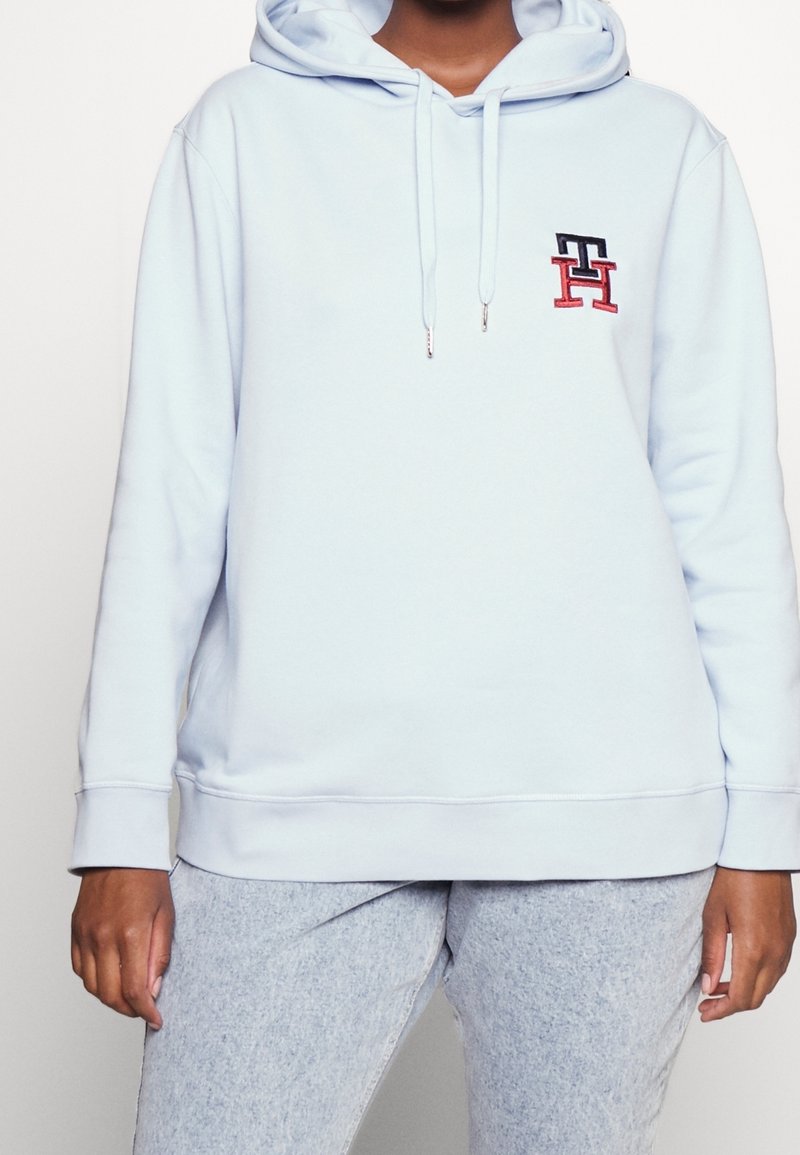 Sudadera de color azul claro con un bolsillo canguro en la parte frontal, capucha con cordones y logo bordado en azul marino y rojo. Fabricada con un tejido suave y puños de canalé.