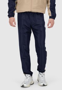 Pantaloni da jogging navy con cintura elastica, caratterizzati da un logo sull'anca e dettagli beige lungo le cuciture laterali, realizzati in un materiale morbido.