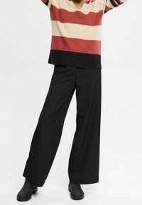 Gestreifter Pullover in Creme, Rot und Schwarz; weit geschnittene schwarze Hose; lässige schwarze Stiefel; lockerer Schnitt und leichter Stoff.