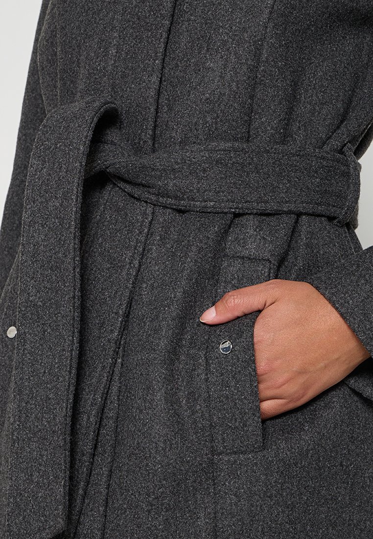 Grau melierter Wollmix-Mantel mit einem Bindegürtel, der eine genoppte Textur und eine seitliche Tasche aufweist. Enthält metallische Druckknopfdetails und feine Nähte.