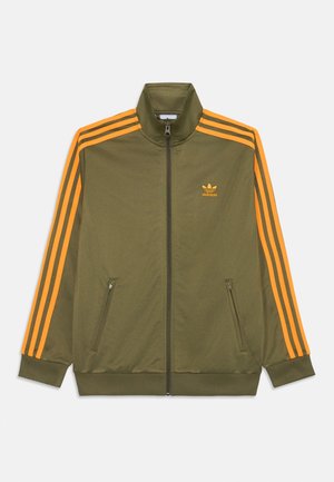 Maslinasto zelena jakna na zip s narančastim prugama duž ramena i strana. Ima visoki ovratnik i rebraste manšete. Mali logo na prsima.