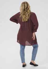 Bordová blůza s volnými dlouhými rukávy; poloprůhledná textura; detail knoflíků na manžetách. Kombinováno se světle modrými skinny džíny a černými balerínami.
