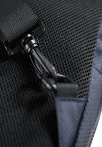Svart mesh-stoff med en teksturert overflate, med en svart plastspenne og stropp. Glatte, mørkeblå detaljer synlige i bakgrunnen.