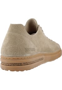 Beige semsket sko med teksturert overflate, avrundet form og kontrasterende gummisåle. Diskret logo detalj på hælen.