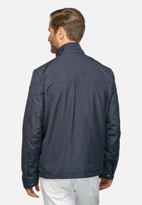 Manskava navyjacka med hög krage, slät textur och knappdetaljer, med en enkel, modern design och skräddarsydd passform i ryggen.