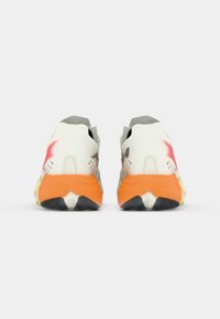 Zapatillas deportivas en blanco y gris con una suela naranja, que presentan un diseño texturizado y acentos en contraste, vistas desde la parte trasera.