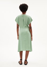 Zielona midi sukienka z krótkimi falbaniastego rękawami, prostym krojem i zapięciem na suwak z tyłu. Gładki materiał z delikatnym blaskiem. Czarne sandały na paski.