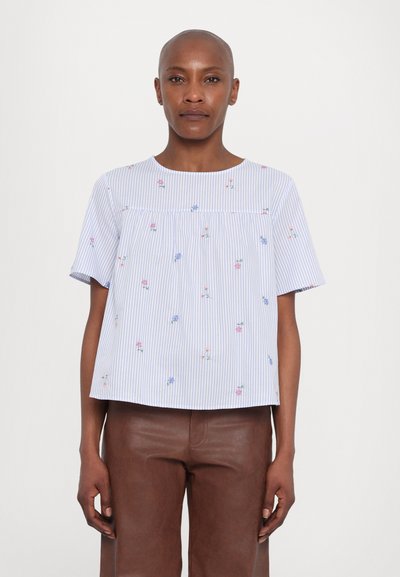 Korte mouwen, gestreept shirt in lichtblauw met bloemenborduursel. Loose fit, ronde halslijn en gebogen zoom. Gepaard met een bruine leren broek.