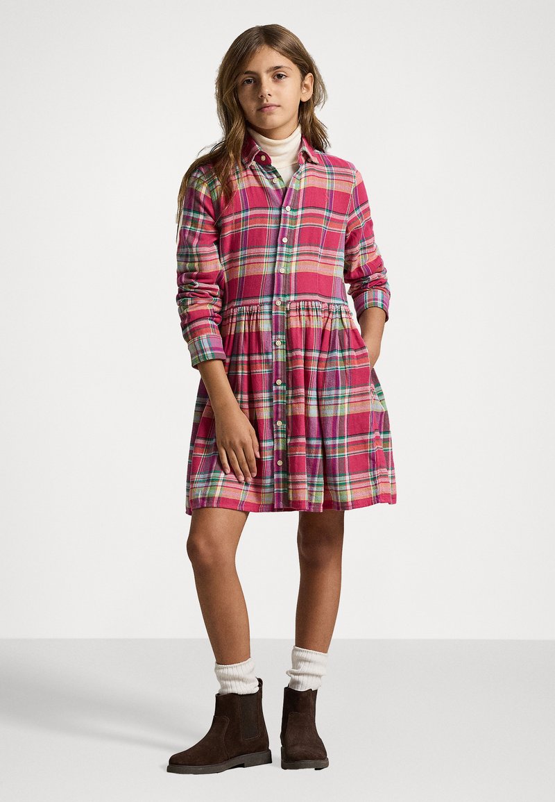 Karirana obleka v roza barvi, z dolgimi rokavi, gumbom spredaj in nabranim pasom. Nosi se z belimi nogavicami in rjavimi gležnjači.