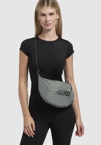 Geantă de umăr din nylon gri cu logo strălucitor "KHUJO 2001", în formă de semilună, cu curea ajustabilă, purtată pe cruce.