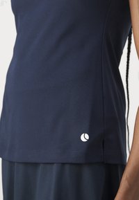 Sportowy top w kolorze granatowym wykonany z fakturowanego materiału. Posiada małe białe logo na dole po prawej stronie oraz boczne rozcięcia zapewniające swobodę ruchów.