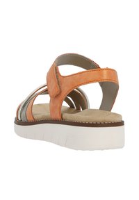 Sandale en cuir orange et argent avec une semelle intérieure rembourrée, une sangle ajustable et une semelle blanche épaisse, mettant en valeur des accents métalliques et un design élégant.