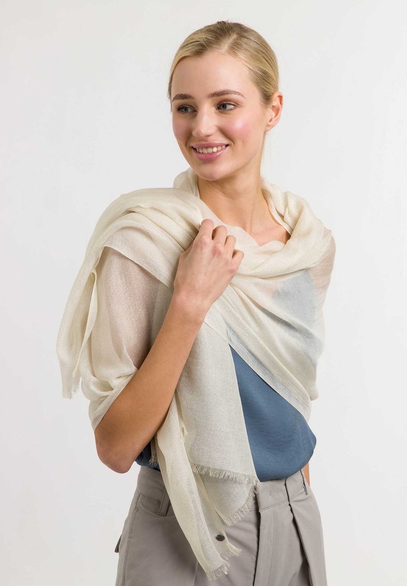 Lightweight, cream-colored scarf with a semi-sheer texture and frayed edges, draped casually over a blue top, creating layered effect.