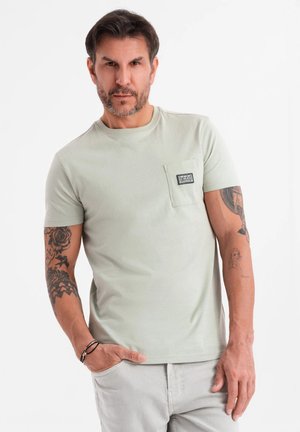 Camiseta de manga corta verde claro con un bolsillo en el lado izquierdo del pecho, hecha de una tela suave; cuenta con una pequeña etiqueta rectangular en el bolsillo.