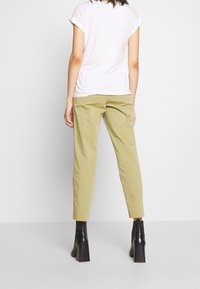 Light pink short-sleeve t-shirt paired with olive green tapered pants and black high-heeled ankle boots, shown from the back.