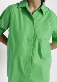 Grön knäppskjorta i slätt tyg, med klassisk krage, korta ärmar och bröstficka.