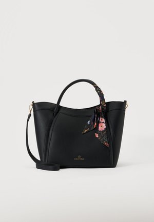 Sac à main en cuir noir avec double poignées, un foulard fleuri noué sur une poignée et une bandoulière amovible sur fond uni.