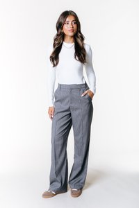 Pantalon large à rayures grises avec poches, associé à une chemise blanche ajustée à manches longues. La tenue présente un design à la fois décontracté et professionnel.