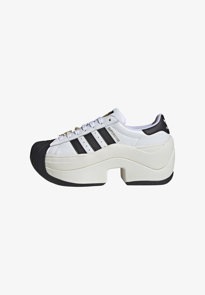 Χοντρά λευκά αθλητικά παπούτσια με μαύρες λεπτομέρειες, διαθέτουν τρία ριγέ σχέδια, στρογγυλεμένη μύτη, μοναδική παχιά σόλα και διακοσμητικές θηλιές για τα κορδόνια.