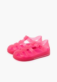 Bright pink plastic sandals with crisscross strap design and adjustable buckle. Open sides for ventilation and textured footbed for grip.