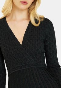 Schwarzes Wickelkleid aus strukturiertem Stoff mit gemustertem Finish, tiefem V-Ausschnitt, langen Ärmeln und plissierter Unterseite.