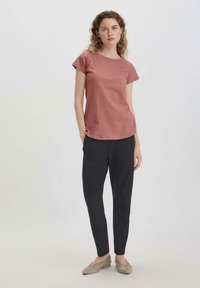 Camiseta de manga corta color óxido combinada con pantalones negros ajustados; el modelo lleva unos zapatos planos color beige; tejido suave y corte relajado.