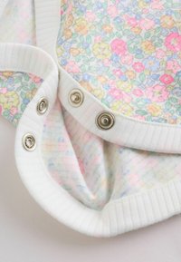 Gros plan sur un vêtement de bébé blanc avec des boutons-pression argentés et un motif floral pastel sur un tissu doux.
