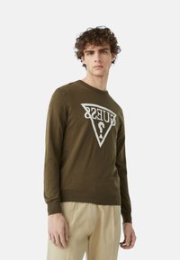 Maglione verde oliva con maniche lunghe, caratterizzato da un grande logo triangolare bianco con testo al centro. Tessuto in maglia morbida e design a girocollo.