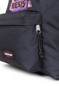 Mochila de tela negra con un bolsillo frontal con cremallera, que cuenta con un tirador de cremallera plateado y una superficie texturizada, marcada con un parche de logotipo de Eastpak.