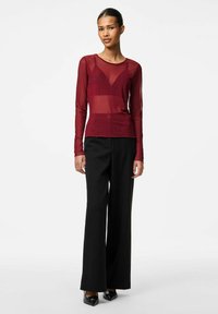 Burgundy långärmad mesh-top med rundad hals, i kombination med svarta vida byxor och svarta spetsiga klackar. Subtila texturdetaljer.