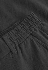 Black elastic waistband with gathered texture, soft fabric surface, and stitched detailing along the edges. Close-up view of design features.
