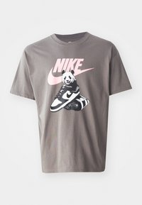 Grå bomulls t-skjorte med et grafisk trykk av en panda som sitter på Nike sko, med en rosa Nike-logo over designet. Korte ermer, rund hals.