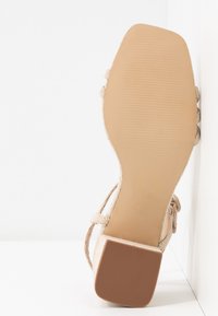 Sandale beige avec semelle texturée et petit talon carré, vue de dessous sur fond blanc.