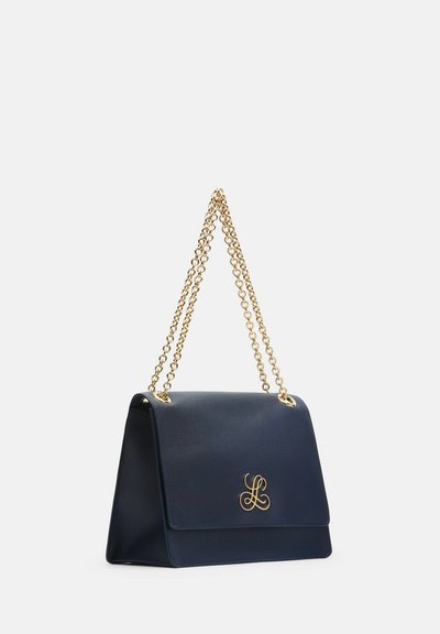 Sac à main en cuir bleu marine avec bandoulière chaîne dorée et emblème décoratif en or sur le rabat avant, présenté de profil oblique.