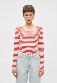 Κόκκινη και λευκή ριγέ μακρυμάνικη μπλούζα με στρογγυλή λαιμόκοψη, συνδυασμένη με ανοιχτό μπλε ψηλόμεσες τζιν παντελόνες με λεπτομέρεια κορδονιού.