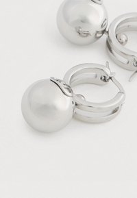 Egy pár ezüst fülbevaló, mindkettőn egy nagy, fényes ezüst fémgömb található.