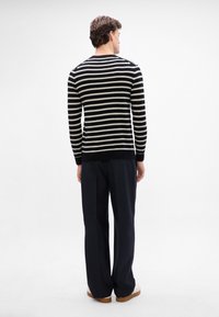Suéter de rayas blancas y negras con mangas largas, diseño ajustado, combinado con pantalones oscuros y tailored y zapatos claros. Vista trasera. Textura suave.