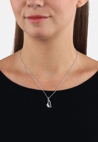 Silverhalsband med en fjärilsberlock, med intrikata detaljer och en glittrande accent, uppvisad på en svart topp mot en neutral bakgrund.