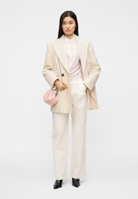 Μπεζ φαρδιά σακάκι, ανοιχτό ροζ μπλούζα και κρεμ παντελόνι με φαρδιά μπατζάκια. Κρατά μικρή ροζ τσάντα με ασημένια αλυσίδα. Μαύρα μυτερά παπούτσια.