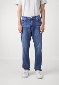 Blue denim jeans with a straight fit, five-pocket design, and slight fading. Paired with a gray t-shirt and white sneakers.