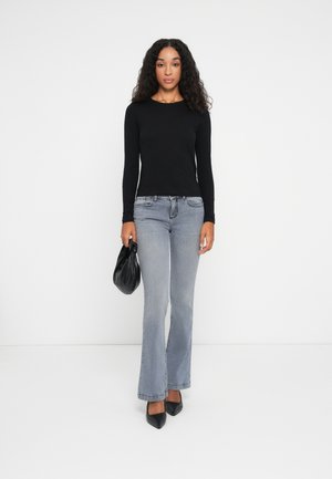 Zwarte lange mouwen top, grijze wijde jeans, zwart puntig hakken, met een zwarte handtas. Glad materiaal met getailleerde en vloeiende vormen.