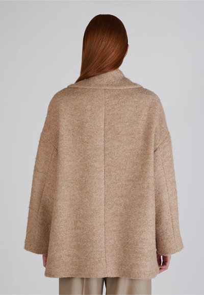 Beżowy płaszcz z mieszanki wełny o luźnej sylwetce, szerokich rękawach i kołnierzu szala. Teksturowany materiał o miękkim, puszystym wyglądzie.