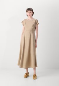 Beige, knee-length dress with short sleeves and a round neckline, made of textured fabric. Paired with light brown, lace-up shoes.