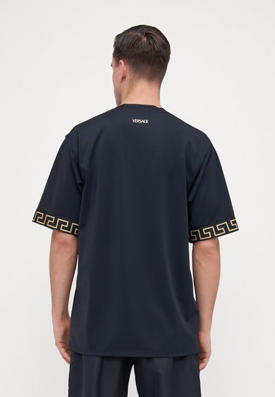 Jūras spēku īsām piedurknēm T-krekls, izgatavots no gludas auduma, ar zelta grieķu atslēgu rakstu uz piedurknēm un diskrētu logotipu mugurpusē.