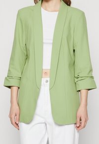 Ljusgrön kavaj med skräddarsydd passform, slagkrage och trekvartslånga ärmar, matchad med en vit crop top och vita byxor.