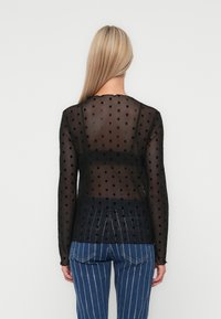Zwart, doorschijnend shirt met lange mouwen en een stippenpatroon, met een ronde halslijn en een getailleerd ontwerp. Gecombineerd met blauwe pinstripe jeans.