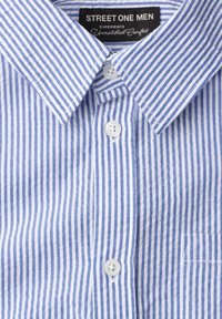 Chemise pour homme à rayures verticales bleu et blanc, avec boutons blancs et une étiquette noire portant la mention « Street One Men » à l'intérieur du col.