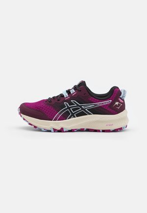 Lila und schwarzer Laufschuh mit weißer und pink gemusterter Sohle, schwarzen Schnürsenkeln und gebrandetem seitlichem Logo, Ansicht von der Außenseite.